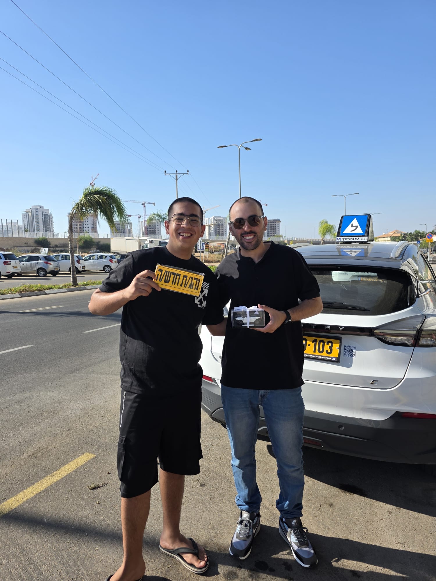 תלמיד עם שלומי שמחון, מורה נהיגה, מחזיק שלט "נהג חדש" לאחר המבחן – תמונה 58