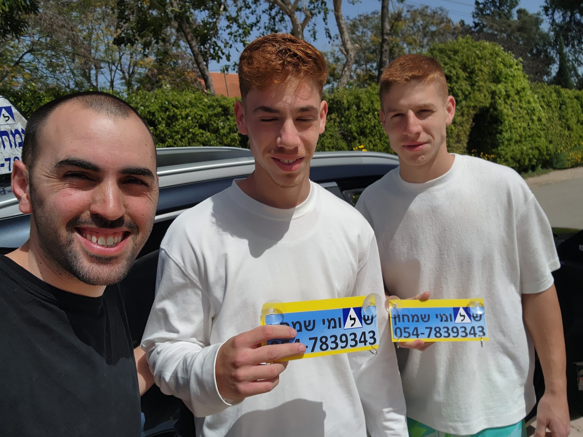 תלמידים עם שלומי שמחון, מורה נהיגה, מחזיקים שלט של בית הספר ביום קבלת הרישיון
